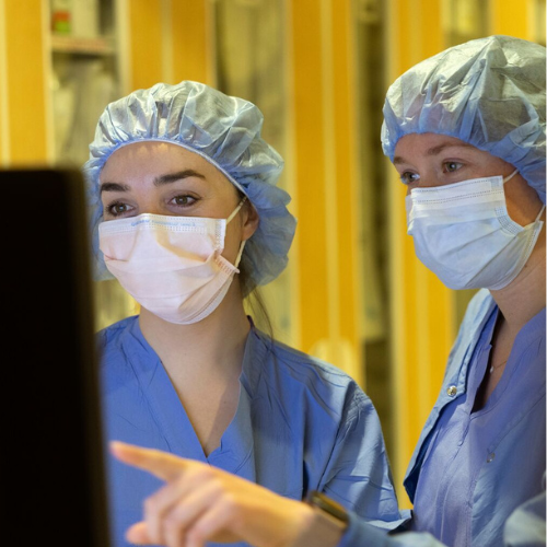 Two healthcare workers in masks and scrubs looking at a monitor.
