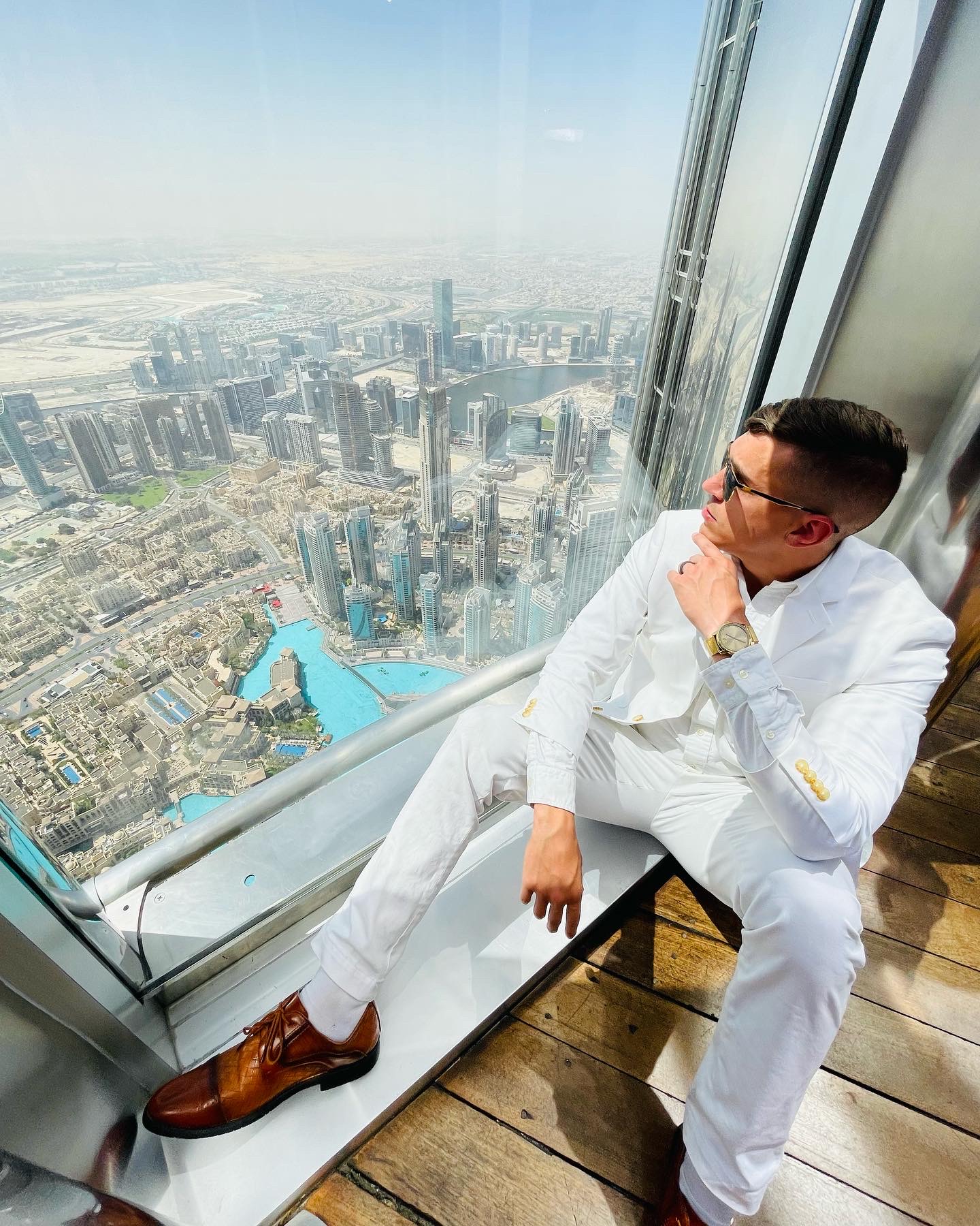Resident Blake Burch in a white suit looking out the window of the Burj Khalifa, United Arab Emirates.