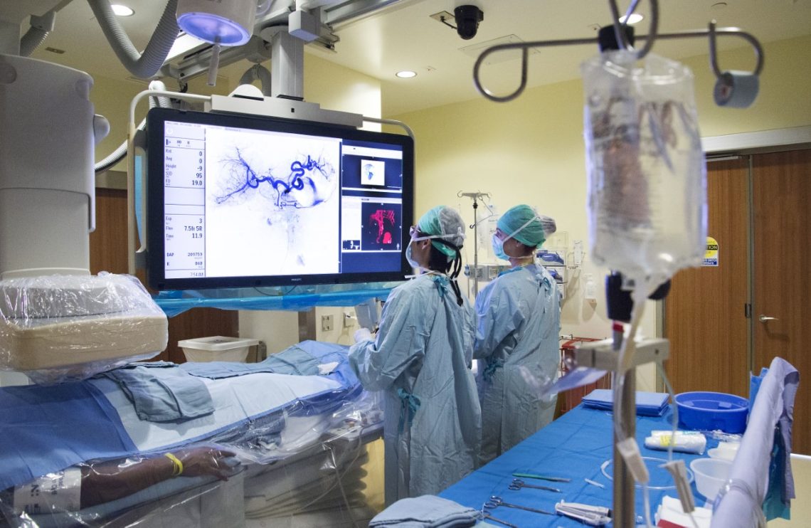 Two vascular surgeons looking at medical images in OR while next to patient.